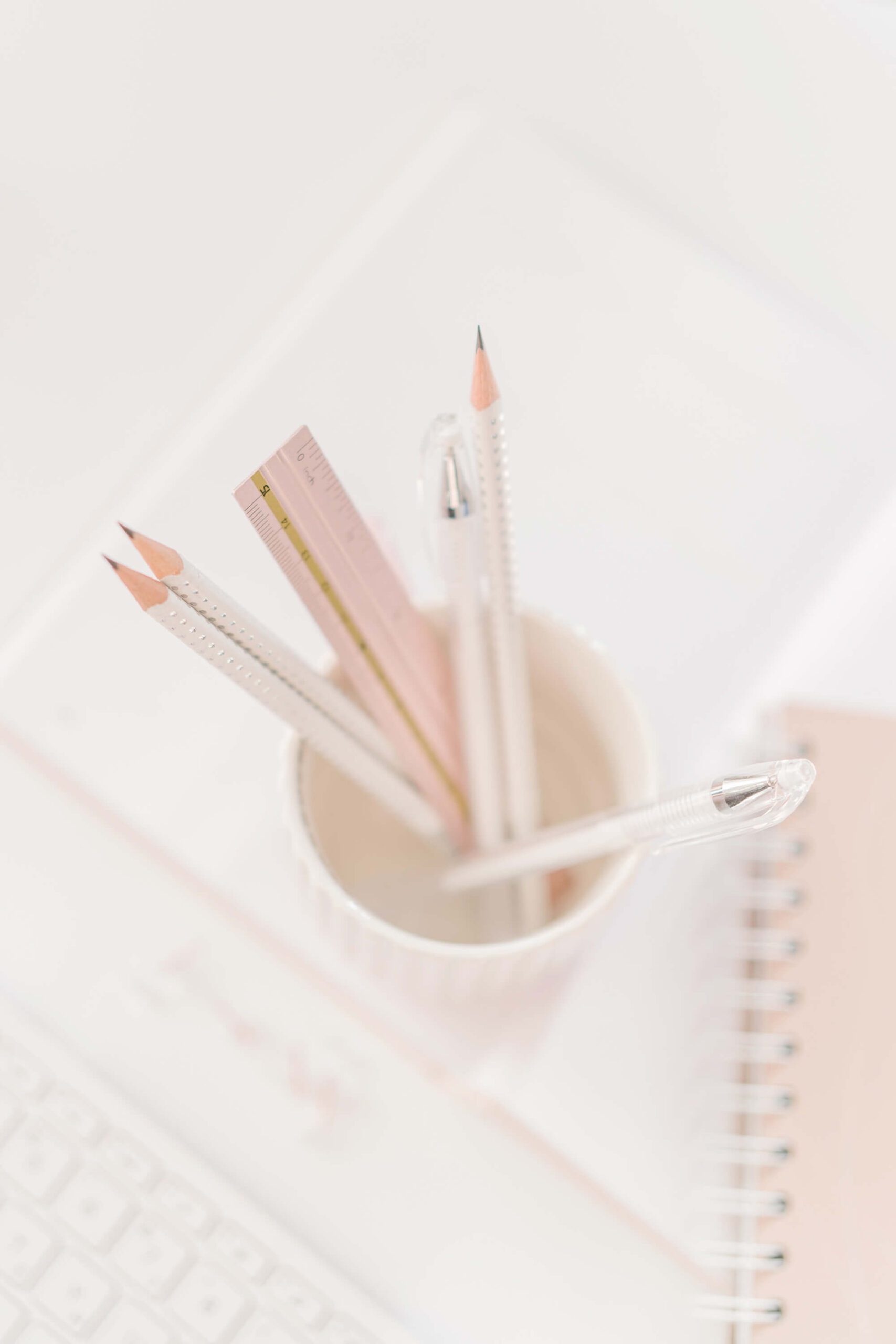 White pencils and blush-colored ruler standing in a white cup on a white desk