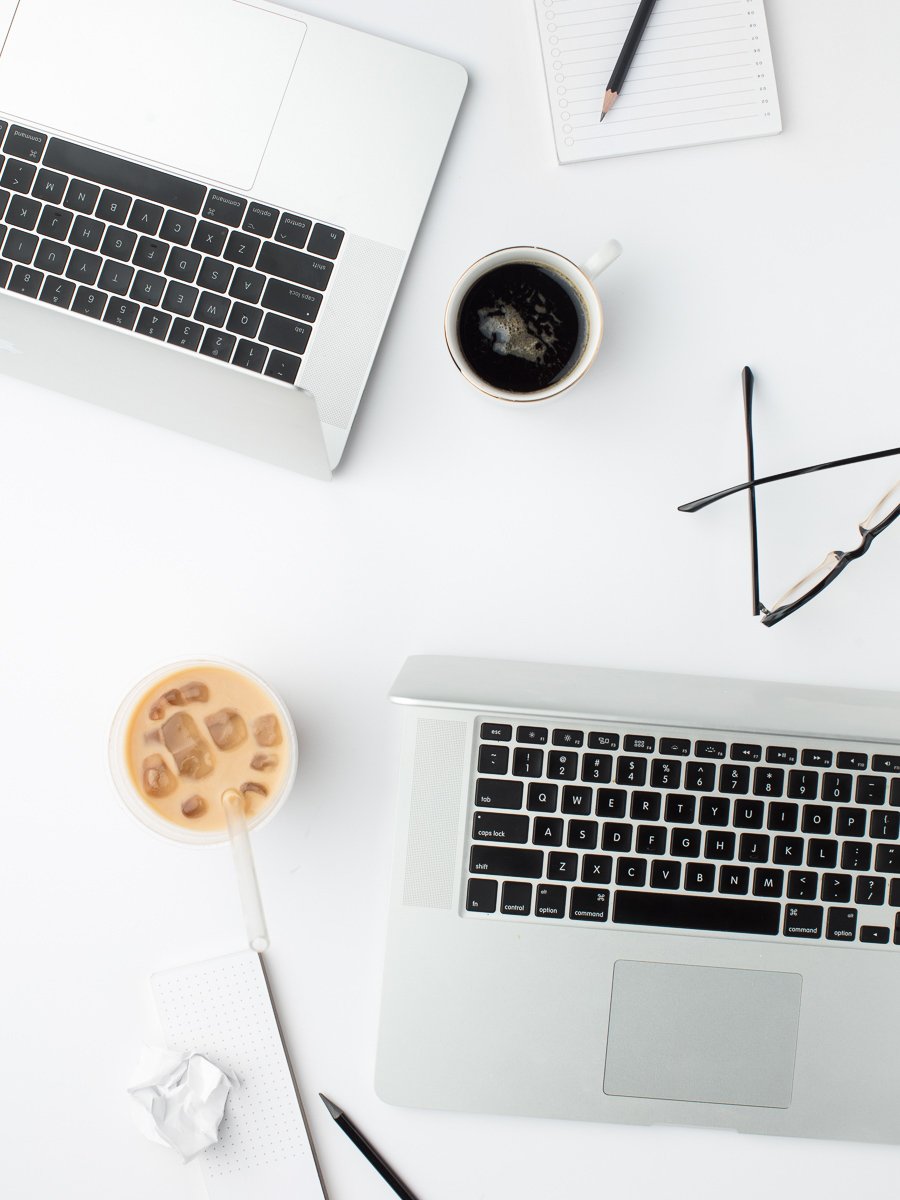Flat lay of two laptops and coffees on a clean, neutral desk.