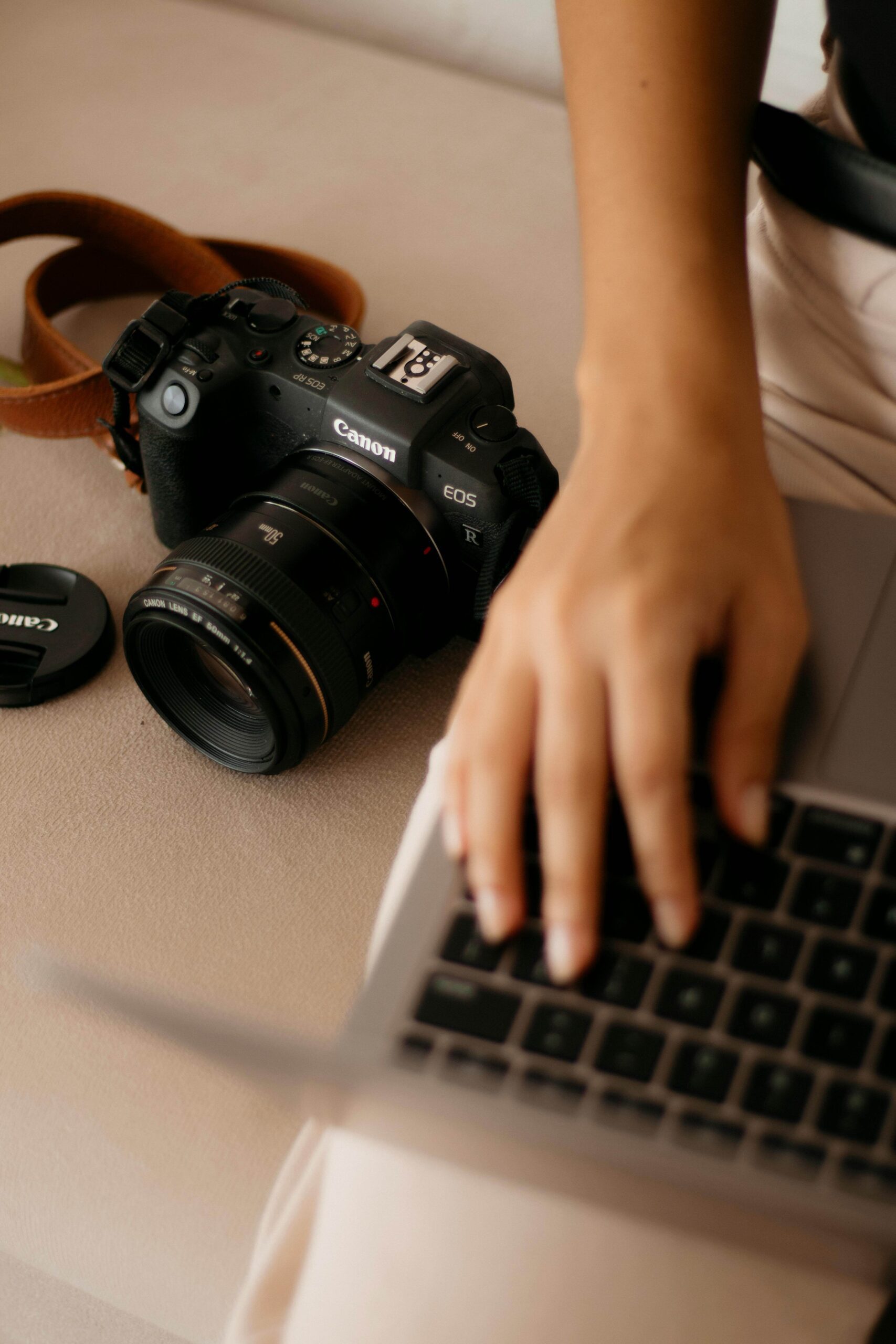 A close-up of a woman’s hand on a laptop with a camera next to her, symbolizing a photographer updating her website and SEO.