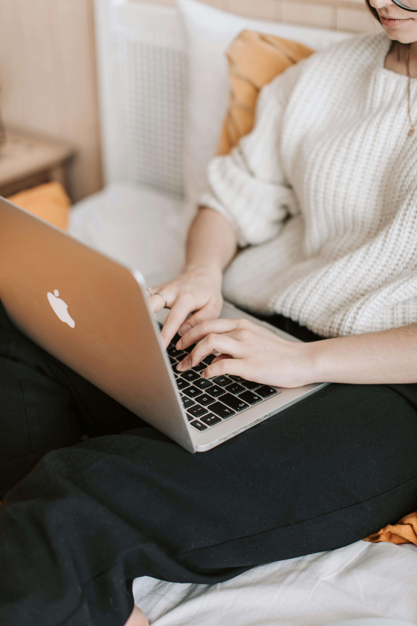 Woman comfortably working from bed with a laptop on her stomach, reflecting a casual, remote work lifestyle common in the wedding industry.